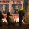 Des personnes portant des manteaux d'hiver assistent à une veillée aux chandelles où Alex Pretti a été tué à Minneapolis. De grandes affiches d'Alex Pretti et Renee Macklin Good sont accrochées sur un mur et des bougies sont posées au sol devant les affiches.