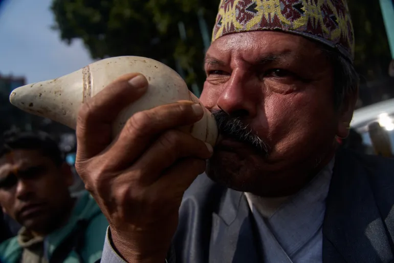 Un partisan souffle une conque alors que les gens se rassemblent pour accueillir l'ancien roi du Népal Gyanendra Shah à son arrivée à l'aéroport international de Tribhuvan à Katmandou, au Népal, le vendredi 13 février 2026. (AP Photo/Niranjan Shrestha)
