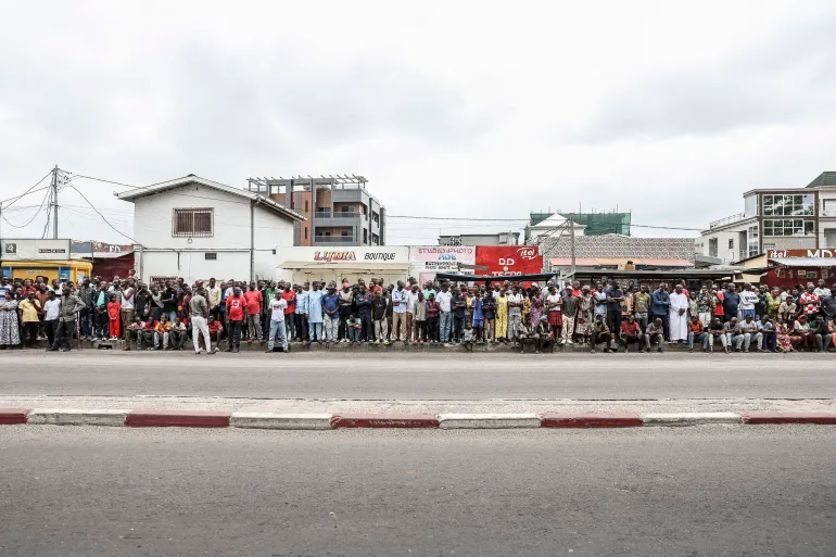 Les partisans du président sortant de la République du Congo et candidat à la présidentielle Denis Sassou Nguesso se tiennent sur le bord de la route alors qu'ils attendent son arrivée dans un bureau de vote à Brazzaville le 15 mars 2026 lors des élections présidentielles de la République du Congo. (Photo de Daniel BELOUMOU OLOMO / AFP)