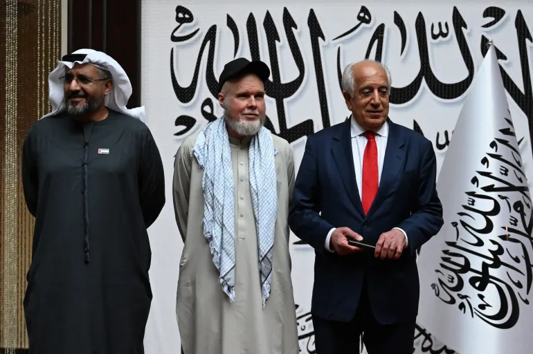 Le citoyen américain Dennis Coyle (au centre) après sa libération par les talibans pose avec l'ancien envoyé spécial américain en Afghanistan Zalmay Khalilzad (à droite) et l'ambassadeur des Émirats arabes unis à Kaboul Saif Mohammed Al-Ketbi (à gauche) à l'aéroport de Kaboul le 24 mars 2026.