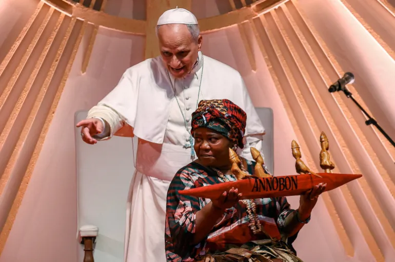 Une femme porte un cadeau pour le pape Léon alors qu'il le montre du doigt en se tenant derrière elle