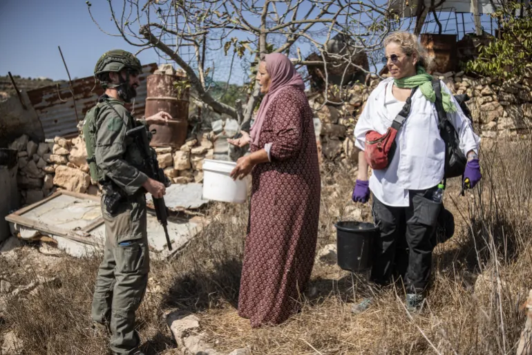 une dame vêtue d'une robe rose et d'un foulard tient un seau blanc et fait face à un soldat armé