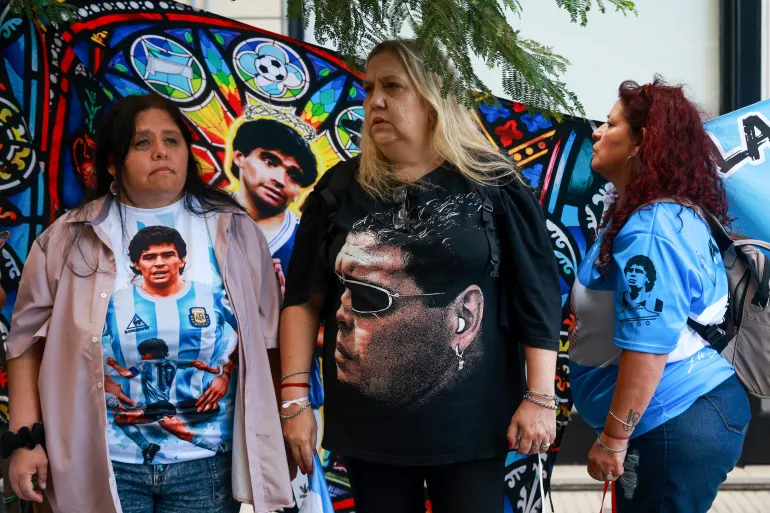 Les supporters de la légende du football argentin Diego Maradona restent devant un palais de justice lors de l'audience préliminaire du procès pour sa mort à San Isidro, dans la banlieue de Buenos Aires, le 14 avril 2026. (Photo de Tomas CUESTA / AFP)