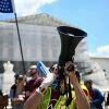 Les manifestants se tiennent devant la Cour suprême des États-Unis. L’un tient un drapeau, un autre un porte-voix et certains tiennent des pancartes.