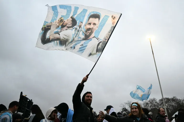 Un fan agite un drapeau portant des images de l'attaquant argentin Lionel Messi près du camp d'entraînement de l'Association argentine de football (AFA) à Ezeiza, dans la province de Buenos Aires, le 20 juillet 2026, en attendant l'arrivée de l'équipe nationale argentine de football des États-Unis après sa défaite en finale de la Coupe du Monde de la FIFA 2026. (Photo de Luis ROBAYO / AFP)